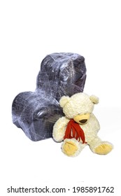 Baby Car Seat Wrapped In Plastic Wrap And A Teddy Bear Closeup On A Light Background