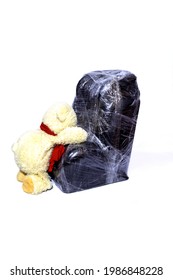 Baby Car Seat Wrapped In Plastic Wrap And A Teddy Bear Closeup On A Light Background