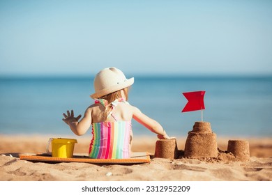 baby child in hat sits on beach against background of sea and plays sand, builds castle. vacation with kids in sunny summer. - Powered by Shutterstock
