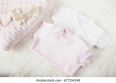 Baby Clothes For A Girl. Baby Jumpsuits, Rompers, Bow Hair Band And Pink Diaper. On A White Fur Carpet. Newborn Baby Concept. Baby Girl Clothes Set