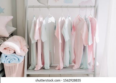 Baby Clothes Hanger In Kid Room Interior Design. Children Romper Suits Folded Soft Linens In Laundry Hamper On Wooden Floor Closeup. Infant Wear Pastel Tones Contemporary Apartment Childcare Concept