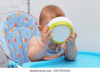 A baby in a colorful highchair eagerly drinking from a bowl, showcasing curiosity and joy during mealtime. The playful lamb-patterned seat adds charm to this candid moment of childhood. - Powered by Shutterstock