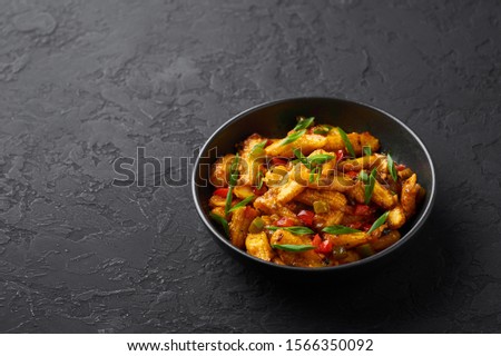 Baby Corn Manchurian dry looks like Schezwan Baby Corn in black bowl at dark slate background. Baby Corn Manchurian - is indo chinese cuisine dish with deep fried corn, bell peppers, sauce and onion.