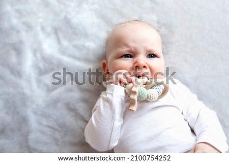 Baby is craying and biting teething ring toy. Theething, first tooth, top view, copy space.