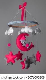Baby crib hanging, Felt cot mobile with stuffed soft stars clouds and moon with sleeping teddy, Cot isolated against neutral grey color background. A cute teddy wearing a pink hat. Baby room decor.