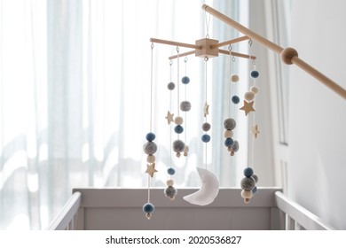 Baby crib mobile with stars, planets and moon. Kids handmade toys above the newborn crib. First baby eco-friendly toys made from felt and wood hanging in light room. Space for text
