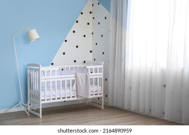 Baby Crib And Standard Lamp Near Color Wall