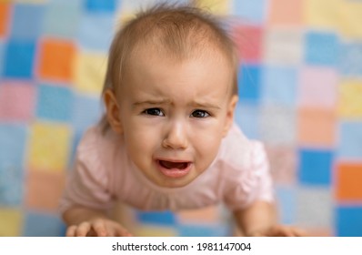 The baby cries standing next to his mother and looking up. A cute, tearful baby. Portrait of a little girl in tears on the background of a colorful blanket. fear in the child's eyes