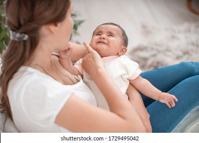 The baby is crying in his mother's arms. A woman tries to calm her small child. Littel girl wants to sleep and eat, fatigue. The newborn has colic and a tummy ache. Teething. Sleeping problem.