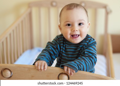 Baby with a cute happy face standing in a cot.