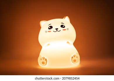 The baby cute kitten-shaped light night lamp with eyes and ears on the bedside table in the dark