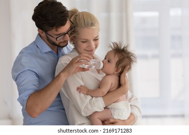 Baby in diaper on parents arms drinks fresh clear water from bottle. Parents keep care of their adorable infant feeling love, spend leisure together at home. Health-care, babyhood, parenthood concept - Powered by Shutterstock