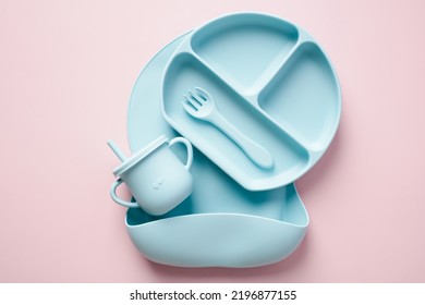 Baby Dishware Set On Color Background. Bib, Cup, Grade Plate, Fork Top View. Baby Self Feeding Utensils