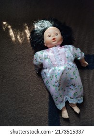 A Baby Doll With Black Hair Lying On A Dark Brown Furry Bed With Black Stripes