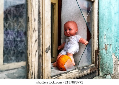 Baby Doll In Window With Broken Glass On Ruined House.