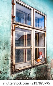 Baby Doll In Window With Broken Glass On Ruined House.