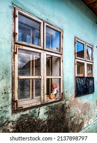 Baby Doll In Window With Broken Glass On Ruined House.