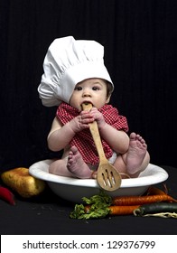 Baby dressed in chef apparel while pressing wooden spoon to his mouth
