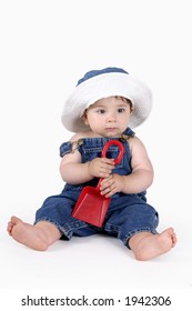 Baby Dressed In Denim Overalls And Matching Sunhat Holding A Spade