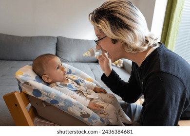 Baby drinking water from a bottle helped by his father at home, the father holding the bottle towards the baby and smile. - Powered by Shutterstock