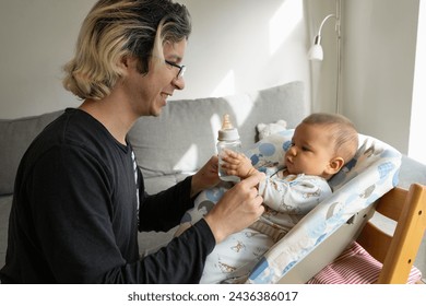 Baby drinking water from a bottle helped by his father at home, holding the bottle high with his hands. - Powered by Shutterstock