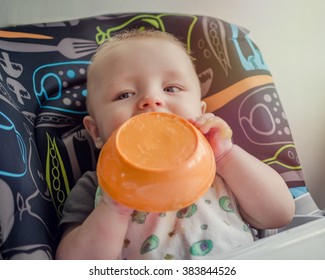 Baby Eating First Solid Food In High Chair From The Plate, Holding It In The Hands. Boy Feeding Himself With Messy Face. Child Having Breakfast, Making Mess At Meal Time. 