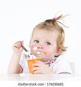 A baby eating yogurt with some on her face.