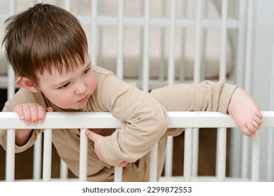 Baby escapes from the crib by climbing over the bars. The child climbs over the railing bed. Kid aged about two years (one year nine months)