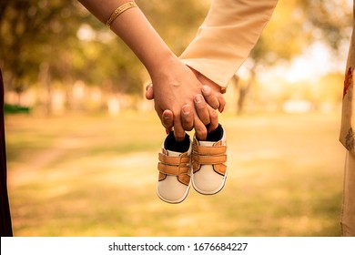 Baby expecting picture with mother and father holding unborn baby shoes, outdoor, garden, parents, family or maternity concept.