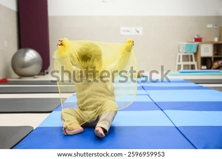 Baby exploring textures and developing sensory skills while playing with a yellow scarf in an early stimulation class