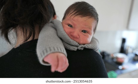 Baby with expressive face looks over mother’s shoulder, close-up shot of parent-child bond in modern kitchen setting, tender moment, newborn baby peeking with curiosity - Powered by Shutterstock