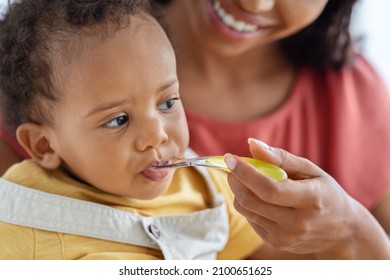 Baby Feeding. Closeup Shot Of Cute Little Black Infant Boy Eating From Spoon, Caring African American Mother Giving Healthy Food To Her Hungry Adorable Toddler Child At Home, Cropped Image