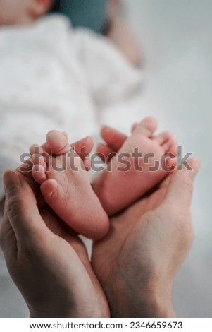 Baby feet cupped into mothers hands. Close-up of tiny, cute, bare feet of a newborn baby boy, girl. Detail of the legs of a newborn. Macro photo of children's legs.