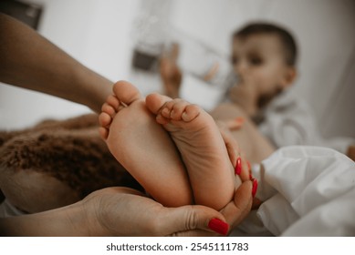 Baby feet lovingly held by an adult s hands, with a child in the background drinking from a bottle. - Powered by Shutterstock