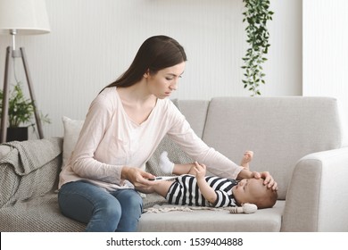 Baby Fever. Concerned Mother Checking Temperature Of Her Sick Newborn Child, Touching His Forehead And Holding Thermometer