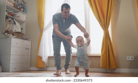 baby first steps. daddy teaches baby toddler son to take first steps. happy family kid dream concept. baby indoors learning to walk father holding child hands. fathers day concept lifestyle - Powered by Shutterstock