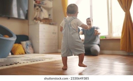 primeros pasos de bebé. el bebé va a su padre por la ventana y aprende a caminar para dar los primeros pasos. concepto de sueño familiar feliz. papá llama a su hijo bebé por primera vez en casa. concepto de vida familiar feliz en interiores