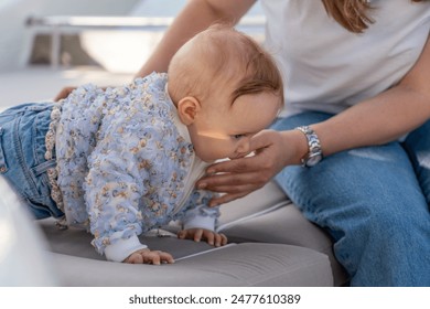 A baby in a floral-patterned jacket crawls towards an adults outstretched hand on a white boat seat - Powered by Shutterstock