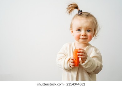 a baby with a food allergy holds a carrot in her hands, the child has red cheeks, irritation