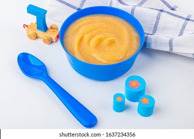 Baby Food. Fresh Homemade Applesauce. Blue Bowl With Fruit Puree On Fabric And Kids Toys On Table. The Concept Of Proper Nutrition And Healthy Eating. Organic And Vegetarian Food. Close Up
