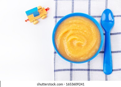 Baby Food. Fresh Homemade Applesauce. Blue Bowl With Fruit Puree On Fabric And Kids Toys On Table. The Concept Of Proper Nutrition And Healthy Eating. Organic And Vegetarian Food. Copy Space For Text