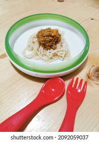 Baby Food Spaghetti Bolognese Using Organic Baby Noodles And Homemade Bolognese Sause With Beef In White And Green Plate With Red Fork Spoon On Wooden Table