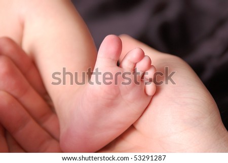Baby foot in mother's hand on black background