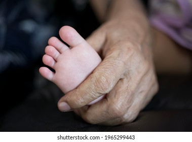 Baby Foot On Old Man Wrinkled Hand, Grandfather Holding Grandchild : Close Up