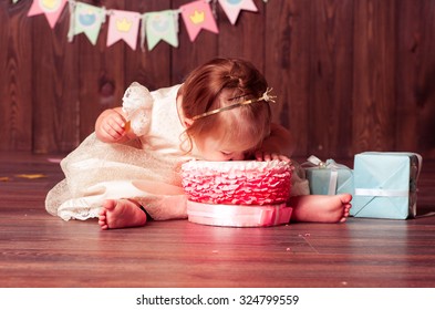 Baby girl 1 year old celebrating first birthday in room. Eating cake. Birthday decoration. Childhood.