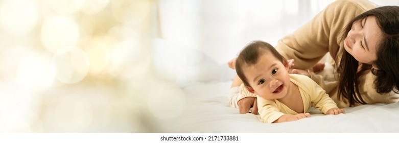 Baby Girl With Asian Mom Smiling Baby Happily Playing Together In Bed In The Bedroom At Home Web Banner With Copy Space On Left