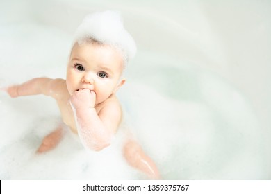 A Baby Girl Bathes In A Bath With Foam And Soap Bubbles