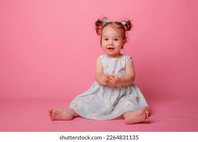 baby girl in a beautiful dress sitting on a pink background