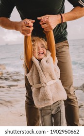 Baby Girl With Blonde Hair, In A Warm Fur Vest. Smiling And Playing With Father. Spring Time, Sun Is Shining On Her Face. Walk Along The Seafront With Family. Travel Abroad. 