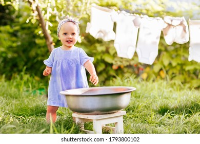 baby girl in blue dress is standing near a basin of water and smiling. - Shutterstock ID 1793800102